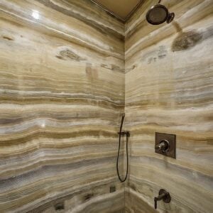 A luxurious shower with onyx walls featuring natural, earthy tones and horizontal veining patterns.